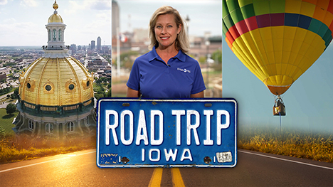 A aerial drone view of the Iowa Statehouse's golden dome with the Des Moines skyline in the background, Brooke Kohlsdorf (host), a multi-colored airborne hot air balloon and Road Trip Iowa logo above a sunlit two lane highway.
