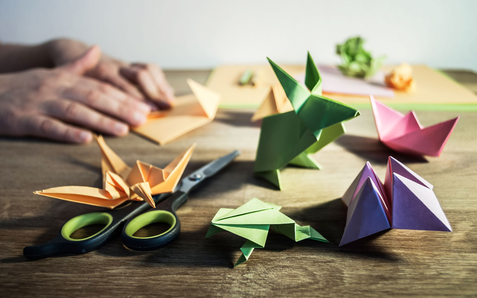 A pair of scissors lie on a table with various animals created out of colored paper