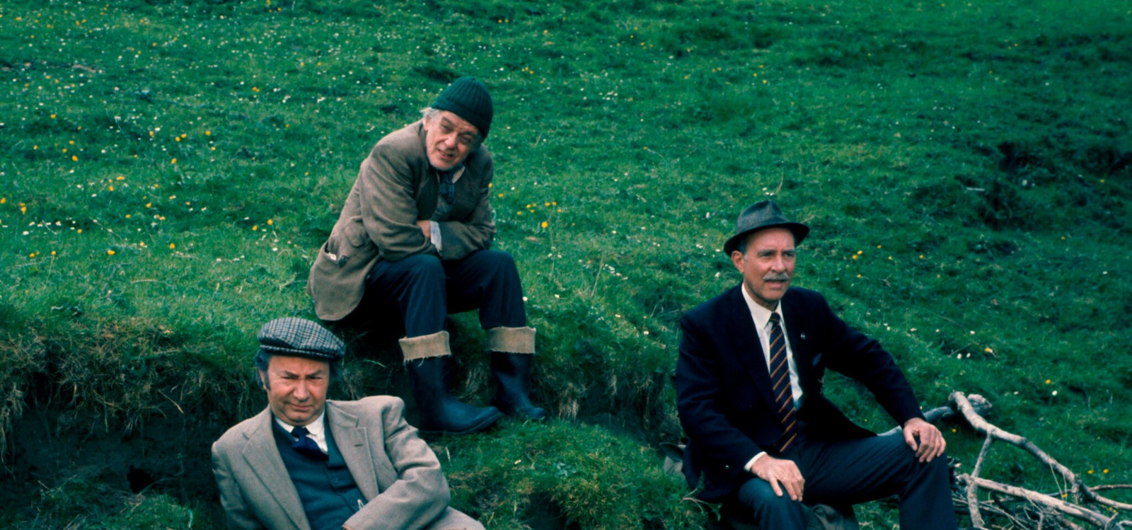 Three men sitting on a grassy hill