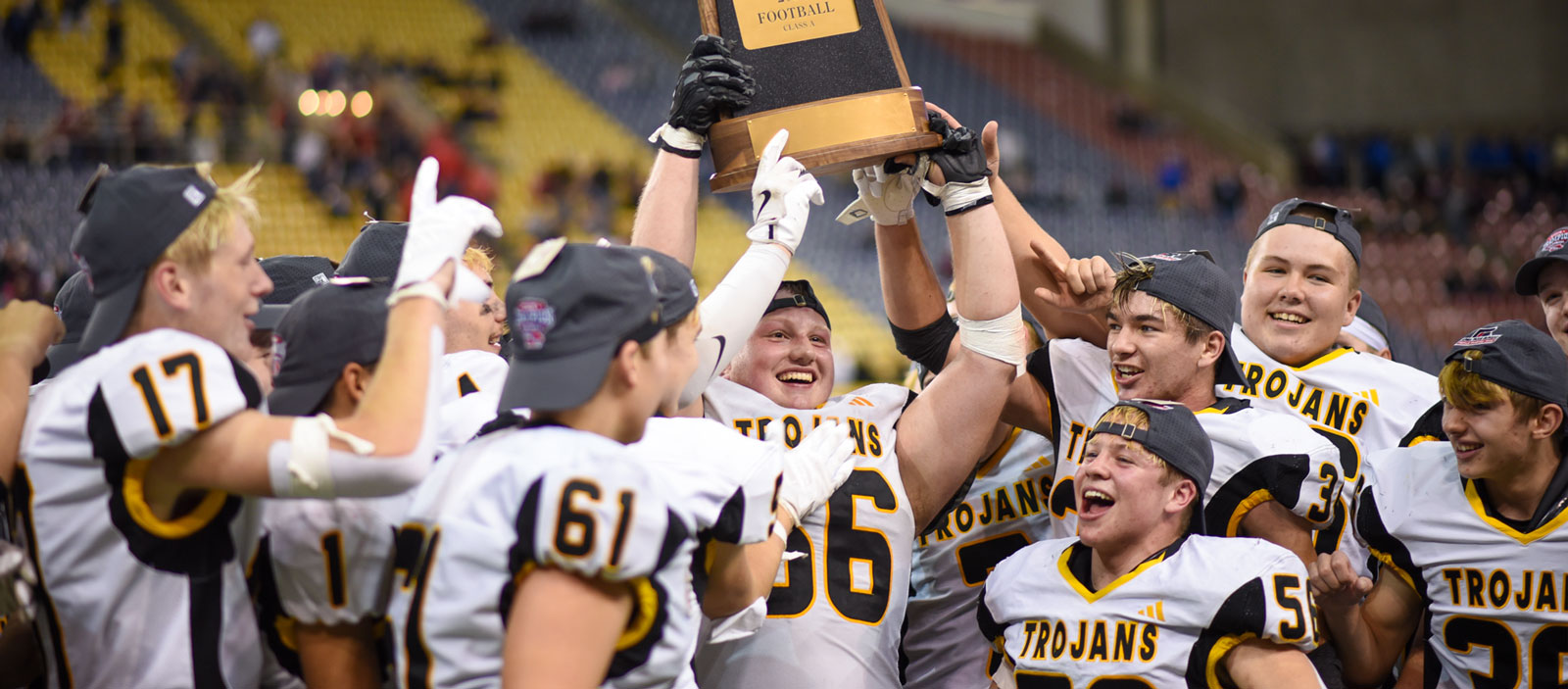 High school football players hold a trophy while celebrating a victory.