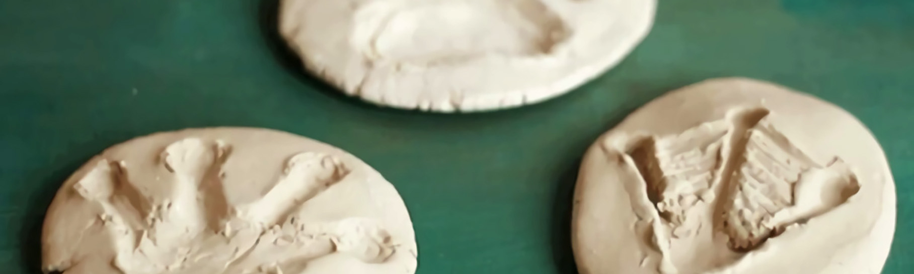 Three flat pieces of clay shaped like a cookie with homemade animal tracks on them.