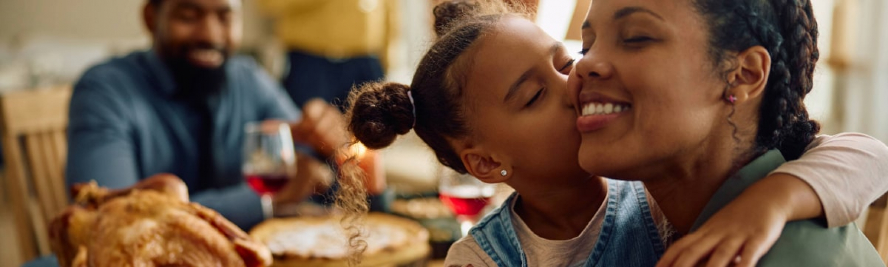 Little girl kissing mom at Thanksgiving dinner