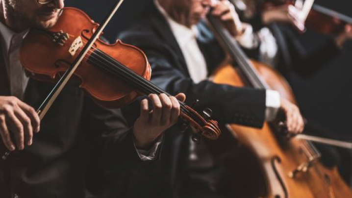 A close up image of a man playing a violin and a large instrument in the background