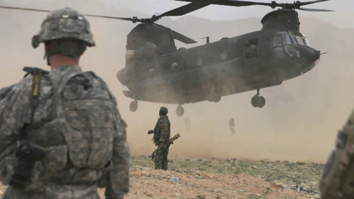 American soldiers standing on the ground as a military helicopter comes in to land.