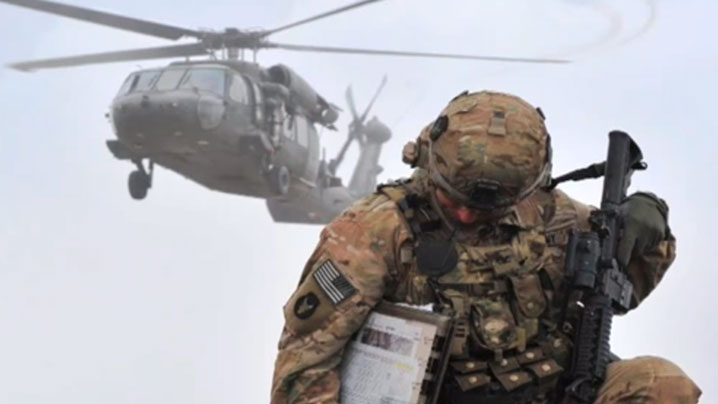 Solider kneeling as a Blackhawk helicopter flies overhead.