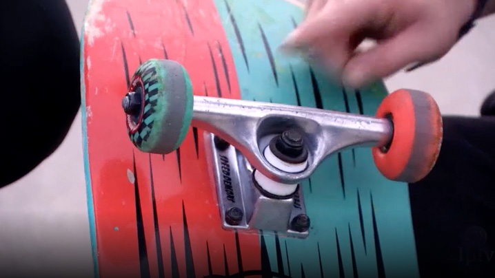 A boy points to the wheels on a skateboard.