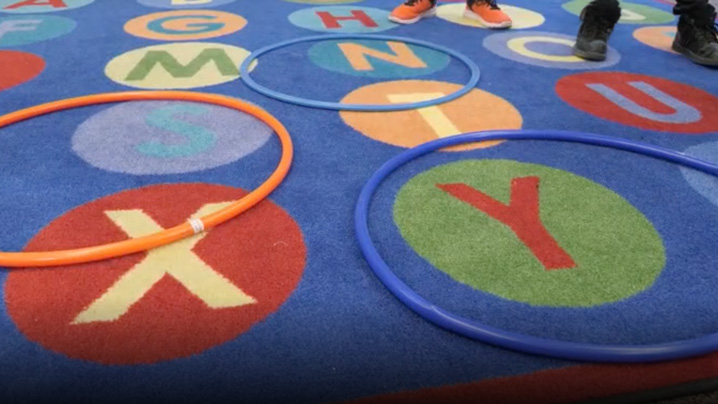 Hula hoops sit on a rug while students stand nearby.