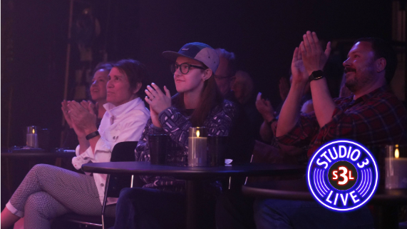 Three people sitting in a dark space like a music club clapping for a musician.