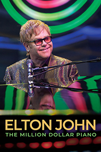 Elton John smiles while performing behind a grand piano.