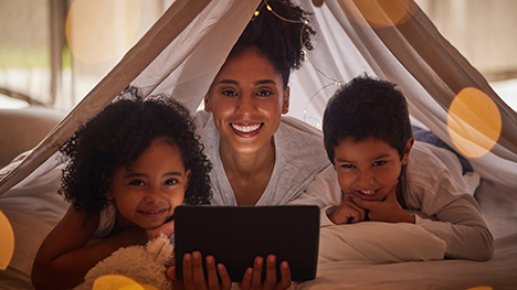 A mother watches PBS KIDS Read-Alongs on a tablet with her young daughter and son.