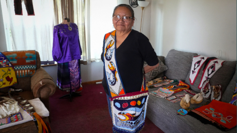 Mary Young Bear standing in her home with her beadwork around her