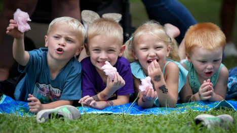 Small kids enjoying cotton candy on a blanket in the grass.