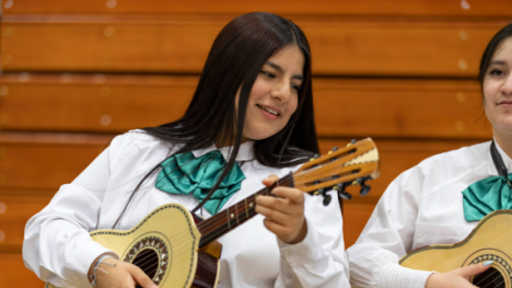 Girl with dark hair in a white shirt playing a guitar