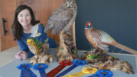 A woman with brown hair poses next to some blue ribbons and three carved wooden birds