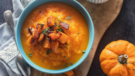 Squash and apple soup in a bowl, displayed on a tray next to a pumpkin