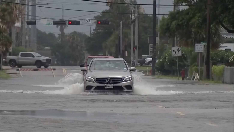 A car drives through a flooded street.