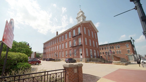 A three-story red brick building with rows of white framed windows is topped with a white cupola