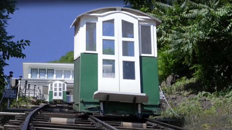 A small green and white outdoor elevator moves a steep hill on railroad type tracks