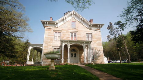 An Italiante-style two-story stone mansion stands on a luscious green lawn