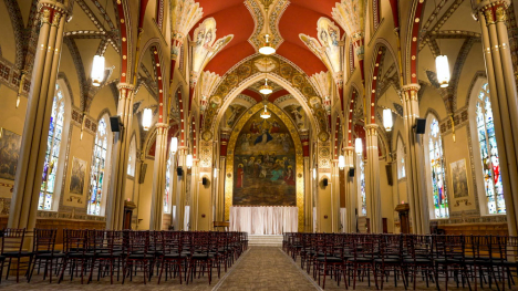 Tall arches support an arched red ceiling forming an aisle that leads to the pulpit and a large Christian mural 