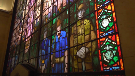 Three soldiers are depicted in a mutli-story stained glass window in brilliant color