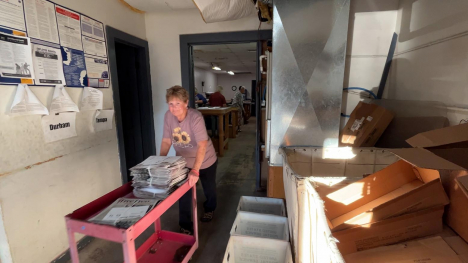 A woman pushes a card of newspapers through a shipping room.